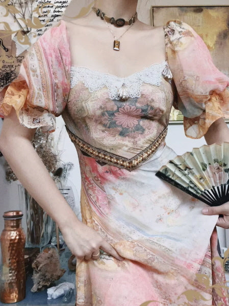 Close-up of a Romantic Fairytale vintage floral maxi dress with puff sleeves, lace-trim neckline, and corset-inspired waist detail, styled as a coquette aesthetic outfit with a hand fan.