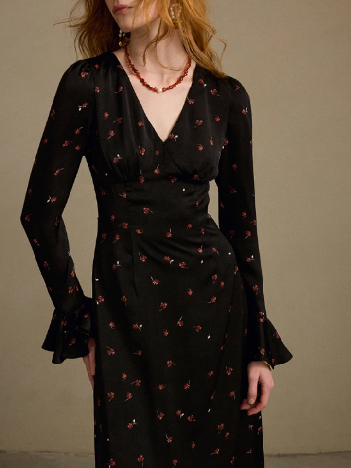 Close-up view of a black V-neck dress with small red floral prints and flared cuffs, showing the elegant vintage-inspired details on the model.