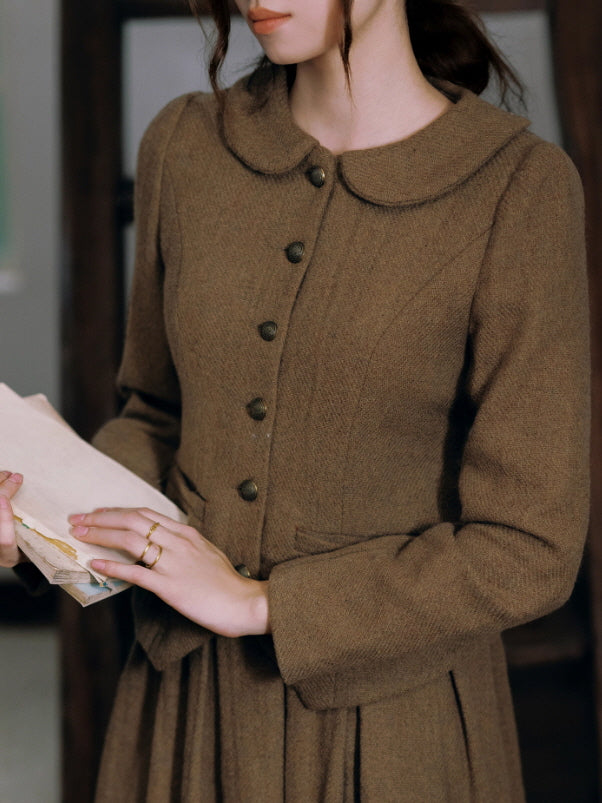 Close-up of a brown vintage jacket with round collar and antique buttons, showing textured fabric and elegant cottagecore detailing as the woman holds old books