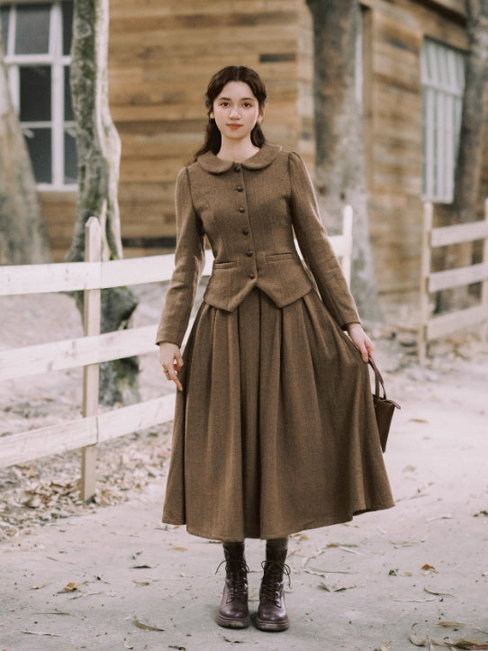 woman wearing a vintage brown jacket and matching pleated skirt, standing outdoors near a wooden fence in a rustic cottage setting, styled with lace-up boots in a classic cottagecore look