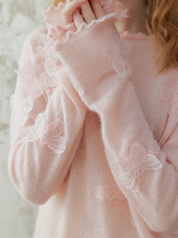 Close-up of a soft pink knit top with delicate butterfly embroidery and scalloped cuffs, styled in a romantic fairycore look.