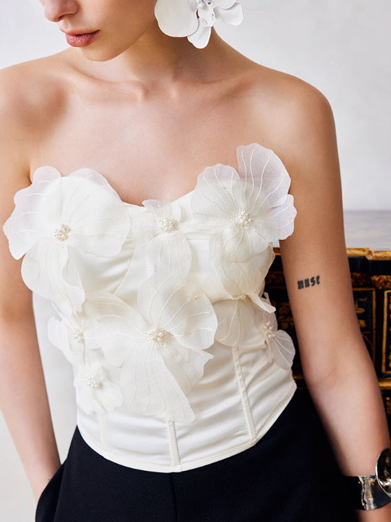 Close-up of a white strapless corset top featuring delicate floral appliqué and pearl embellishments, inspired by vintage romantic and fairycore style.