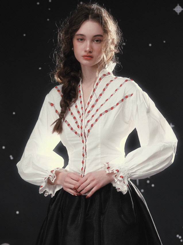 Close-up of an ivory romantic blouse featuring delicate red ribbon embroidery, a softly shaped waist, and lace-trimmed cuffs, capturing a timeless vintage and fairytale aesthetic look.