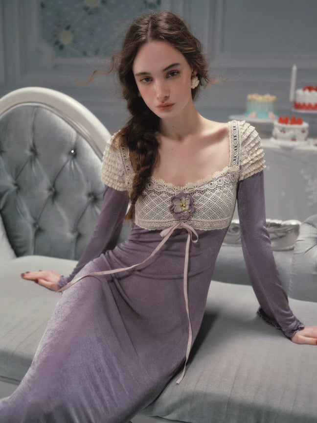Romantic lavender fairycore dress worn by a model sitting on a vintage sofa, featuring a square neckline, delicate lace bodice, floral appliqué detail, and long fitted sleeves in a soft fairytale-inspired interior.