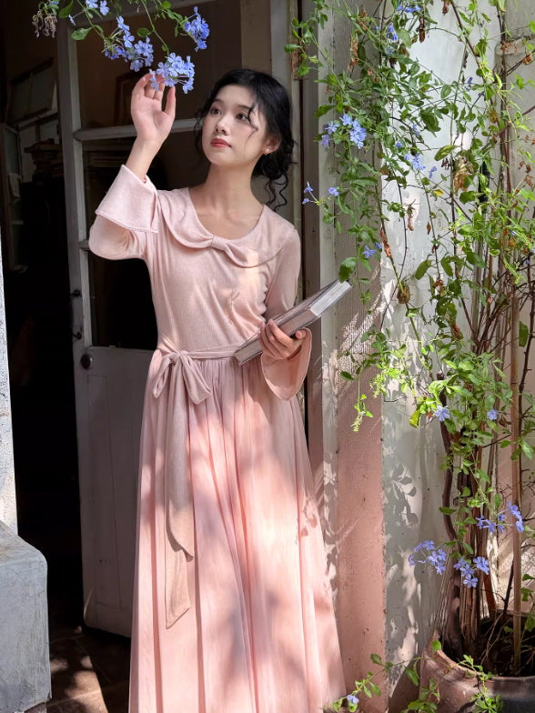 A woman wearing a soft pink knit dress with a sailor collar and waist tie, styled outdoors among flowers, creating a romantic cottagecore and fairycore aesthetic outfit.