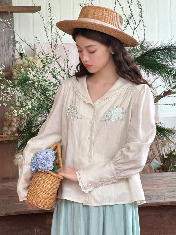 A woman wearing a cream embroidered blouse with a lace-trimmed sailor collar, styled with a straw hat and basket in a garden setting, creating a soft cottagecore and vintage aesthetic outfit.