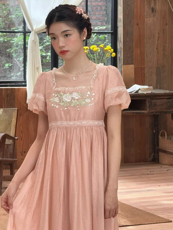 Dainty pink cottagecore dress featuring a square neckline with white lace and short puff sleeves, accessorized with a gold moon necklace.
