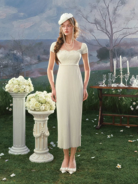 Vintage-inspired white midi dress with square neckline and short sleeves, styled in romantic garden setting with classical decor