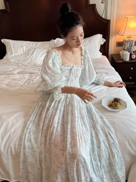 woman wearing light blue floral cottagecore dress sitting on bed, airy romantic silhouette