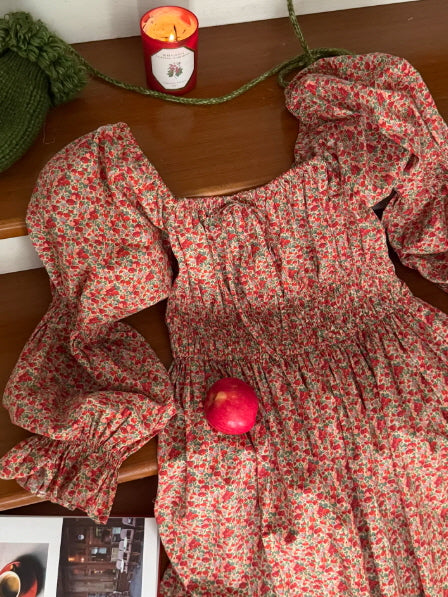 red floral cottagecore smocked dress flat lay with apple and candle, vintage cozy aesthetic