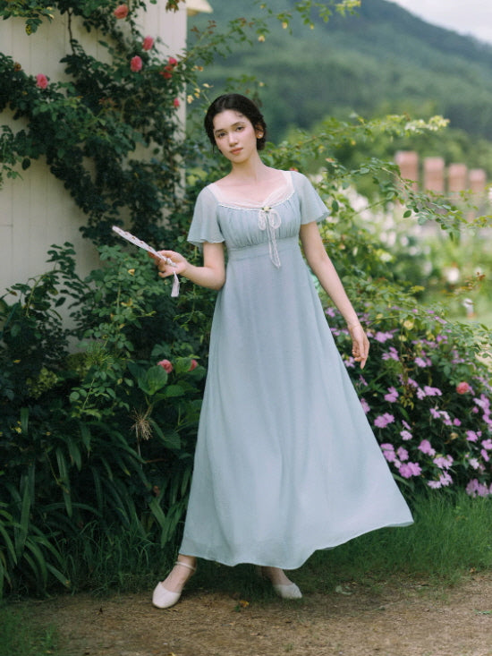 Flowing dusty blue cottagecore maxi dress with empire waist in a country garden