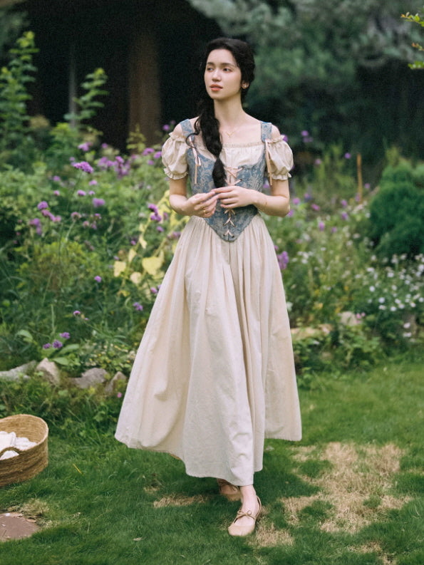 Dreamy prairie style maxi dress with blue floral corset bodice and light beige skirt worn in a flower garden