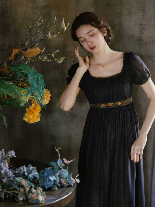 Black gothic romantic dress with puff sleeves, empire waist and delicate floral accents beside an autumn inspired arrangement