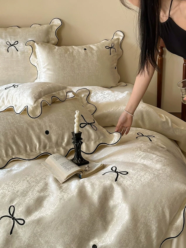 Vintage inspired satin bedding set featuring embroidered bows, black trim, and elegant scalloped pillow shams