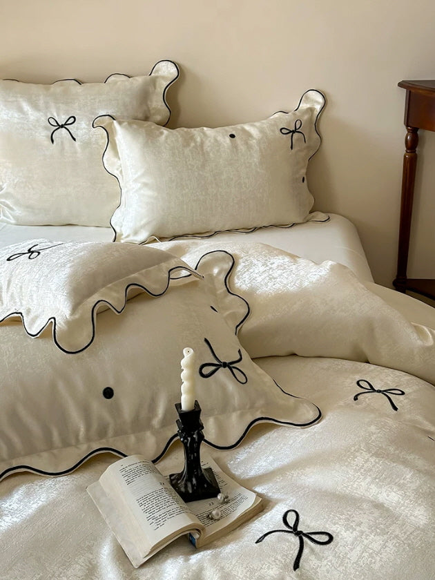 Elegant bow bedding set in creamy ivory satin with contrast black piping and romantic vintage bedroom styling