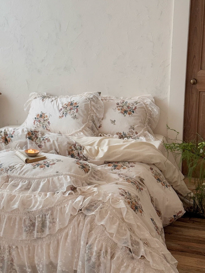 Vintage cottage bedding with delicate floral clusters, lace trimmed pillow shams, and feminine ruffle accents in soft ivory
