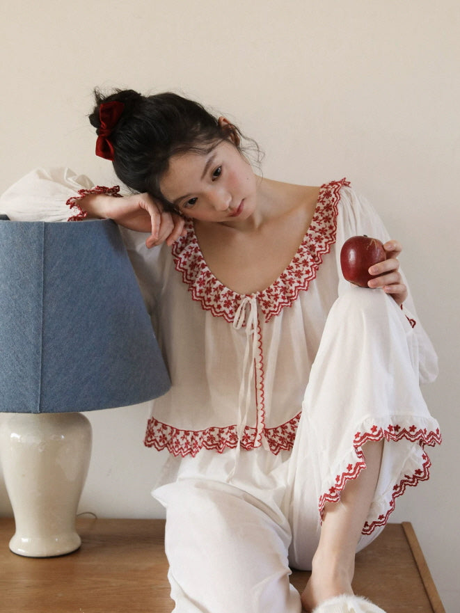 Close up of white pajama top with red floral embroidery and scalloped ruffle neckline
