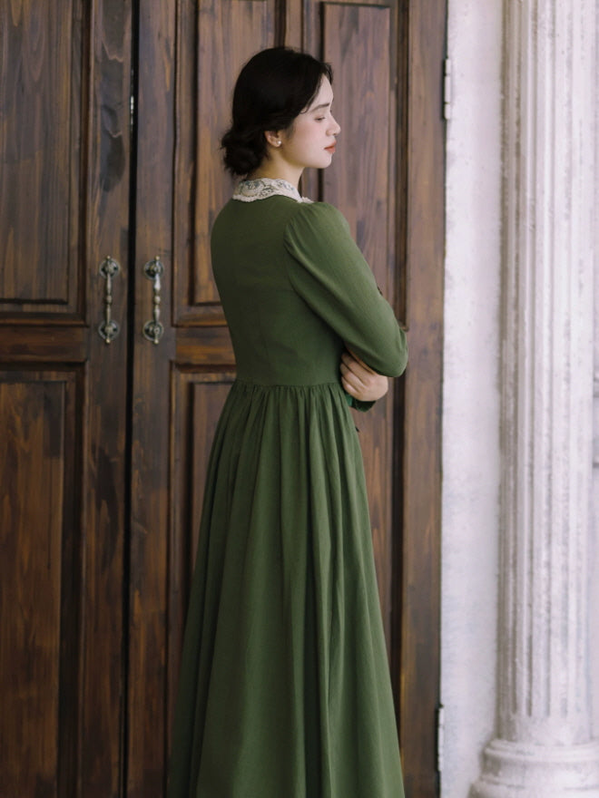 Green vintage-inspired maxi dress with lace-trimmed bodice and ornate white collar, held with an antique book