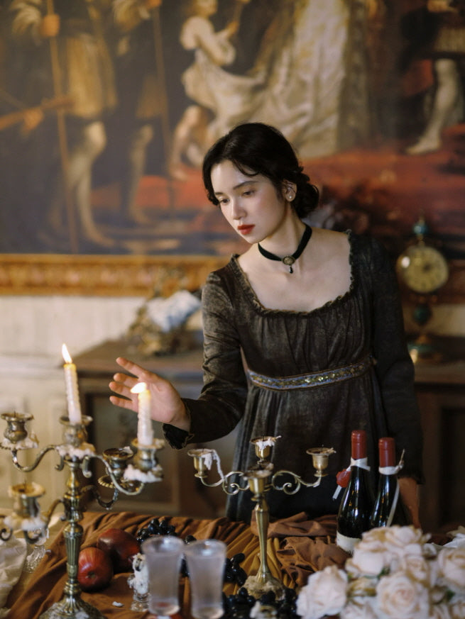 Dark vintage maxi dress with square neckline, long sleeves and embroidered empire waist in a candlelit interior