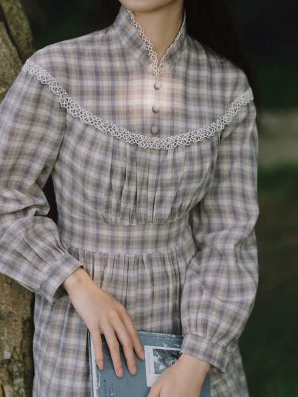 Women’s gray check maxi dress with lace-trimmed neckline and long sleeves styled with a book beside a lakeside boat