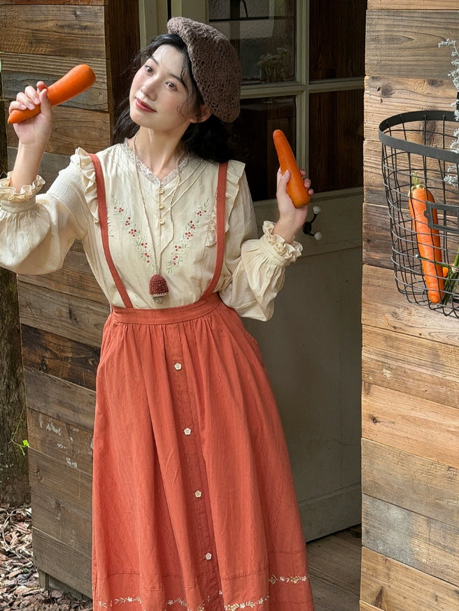 Cottagecore outfit with cream embroidered blouse and rust suspender maxi skirt in a cozy rustic interior