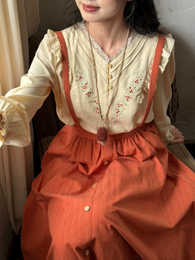 Vintage-inspired embroidered blouse and terracotta suspender skirt styled with a book in a warm cottage interior
