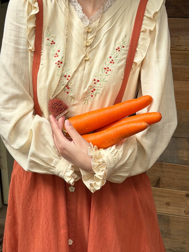 Close-up of cream vintage blouse with floral embroidery, pintuck details and rust suspender straps