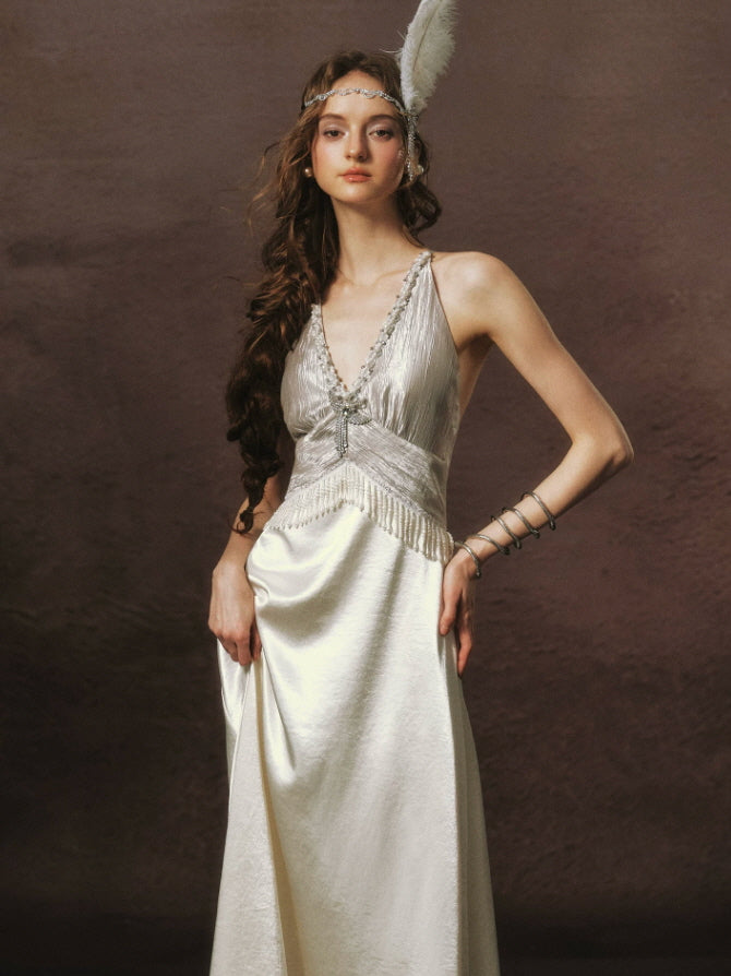 Detailed view of a pearl embellished ivory satin dress featuring a plunging neckline, sparkling brooch, and delicate beaded fringe.