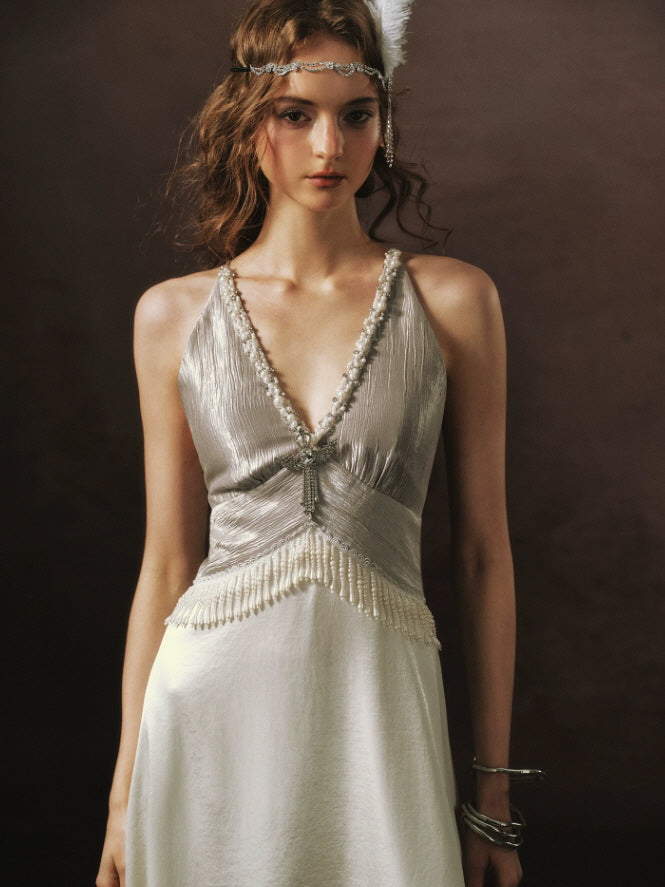 Close-up of a 1920s Gatsby inspired ivory dress featuring shimmering pleated fabric, pearl embellishments, and beaded fringe.