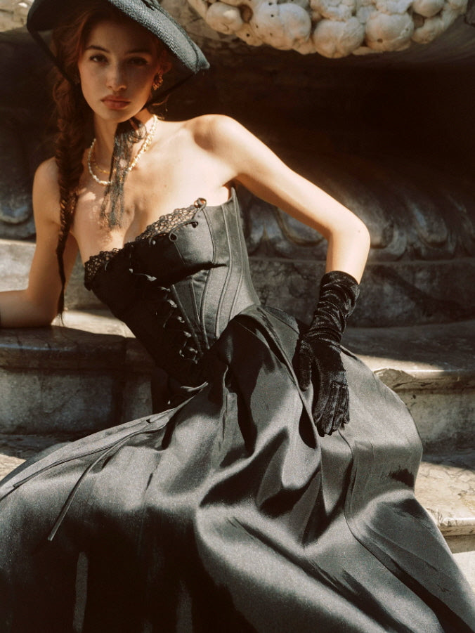 Vintage-inspired black corset midi dress featuring a structured lace-up bodice, elegant strapless neckline, and dramatic flowing skirt.