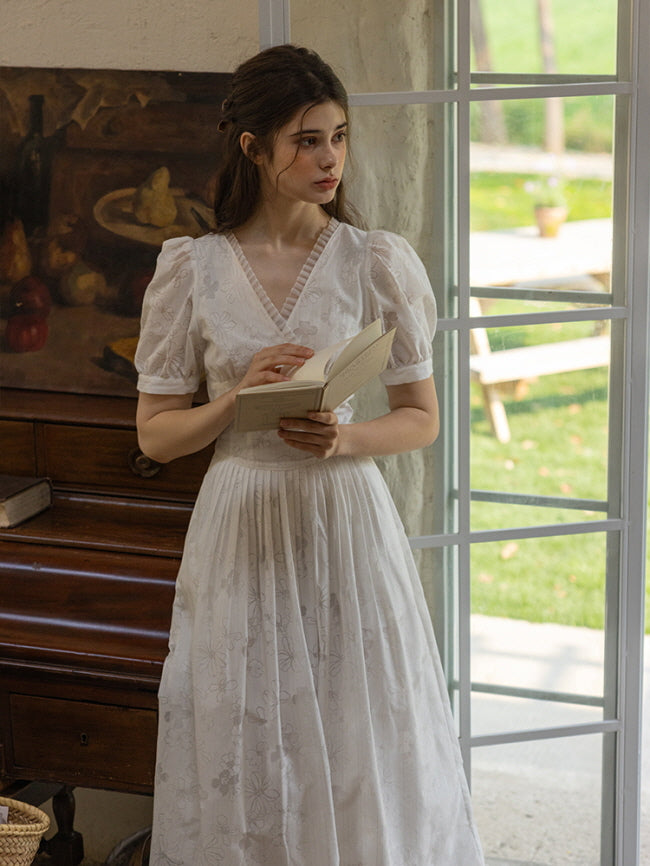 Indoor scene with a young woman reading a book by the window, wearing a white floral dress with puff sleeves and a fitted bodice, exuding a cottagecore aesthetic.
