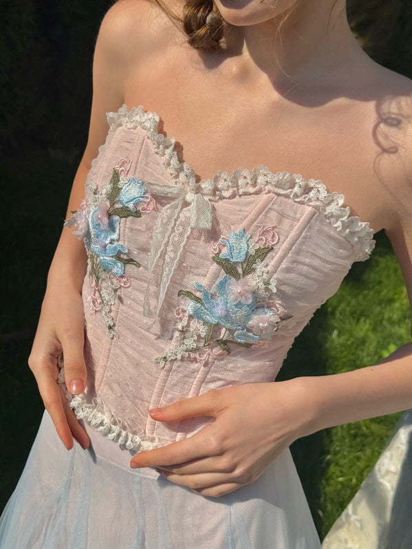 Close-up of pink corset bodice with lace trim and detailed floral embroidery in blue and pink, styled for a soft feminine vintage-inspired look