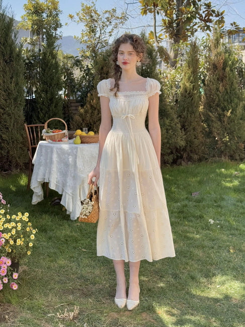 A full-length aesthetic shot of a princesscore outfit featuring a fairytale ivory dress with vintage lace, puff sleeves, and floral embroidery, worn by a woman in a sunlit cottagecore garden.