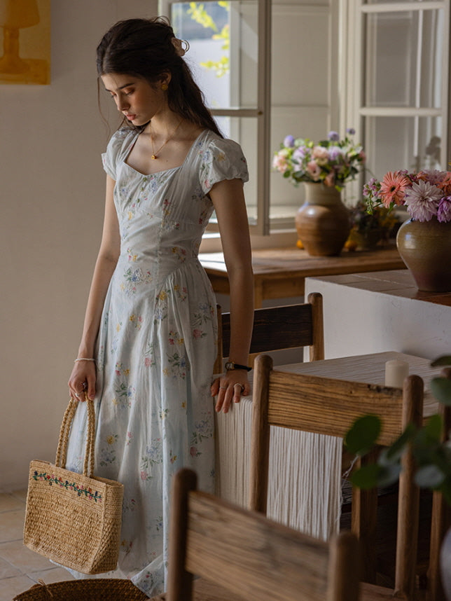 Soft floral dress with cap sleeves and a sweetheart neckline, paired with a woven floral-embroidered tote, styled in a serene cottagecore-inspired kitchen setting with natural wood accents.