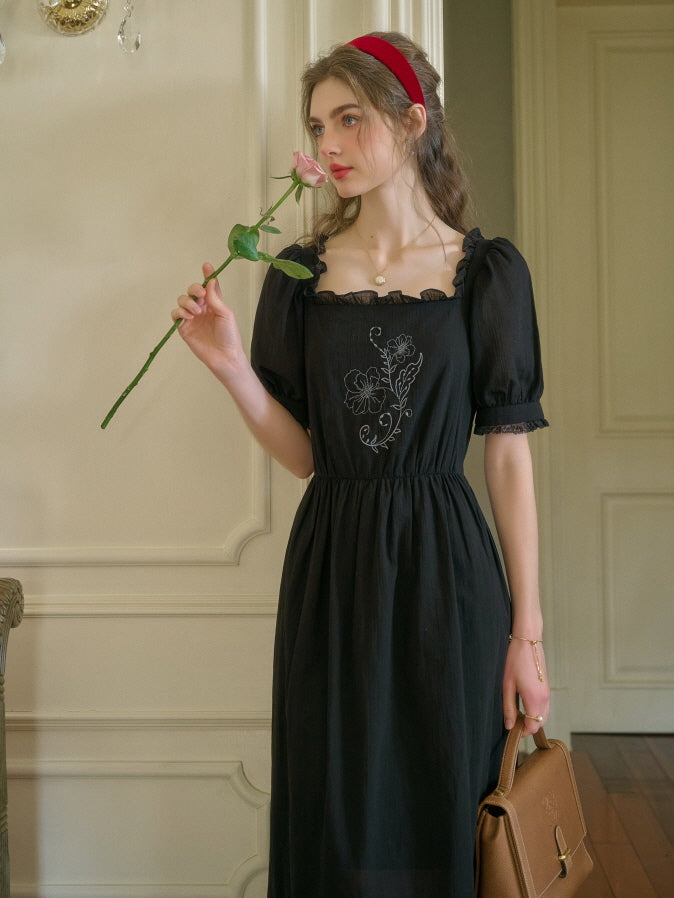 Side profile of a woman in a vintage black retro dress with puff sleeves and floral embroidery, smelling a pink rose while carrying a structured brown handbag.