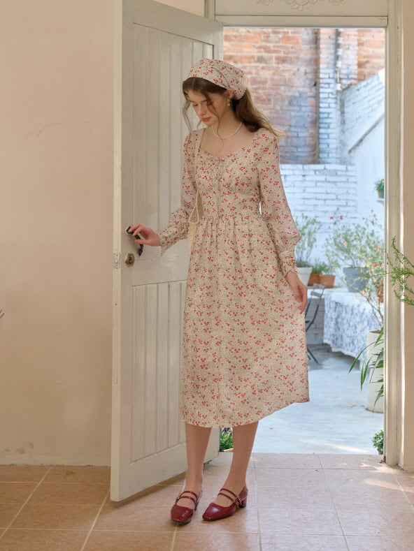 A woman in a romantic cottagecore floral dress and headscarf, standing gracefully near a rustic wooden door with natural light streaming in