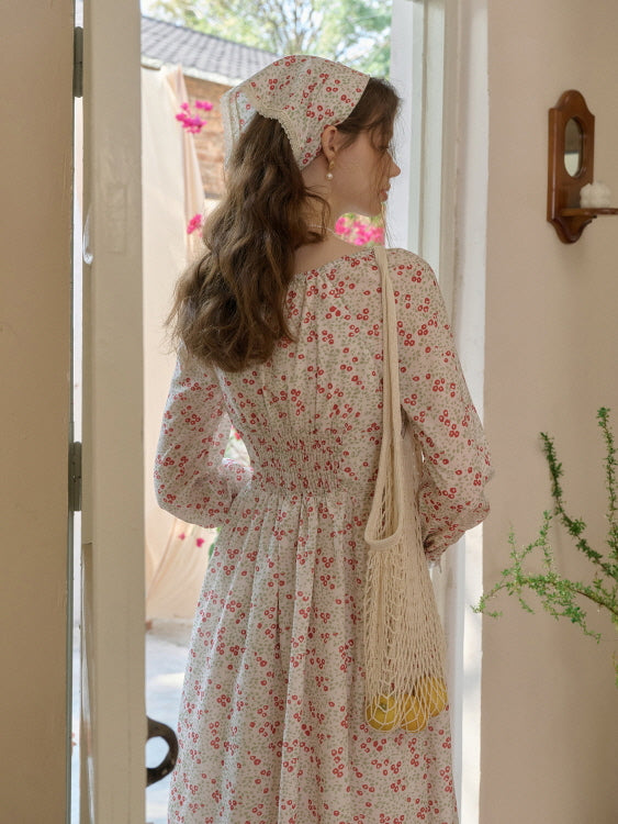 Back view of a retro floral dress with shirred waist detail, accessorized with a lace-trimmed headscarf and a net bag carrying lemons.