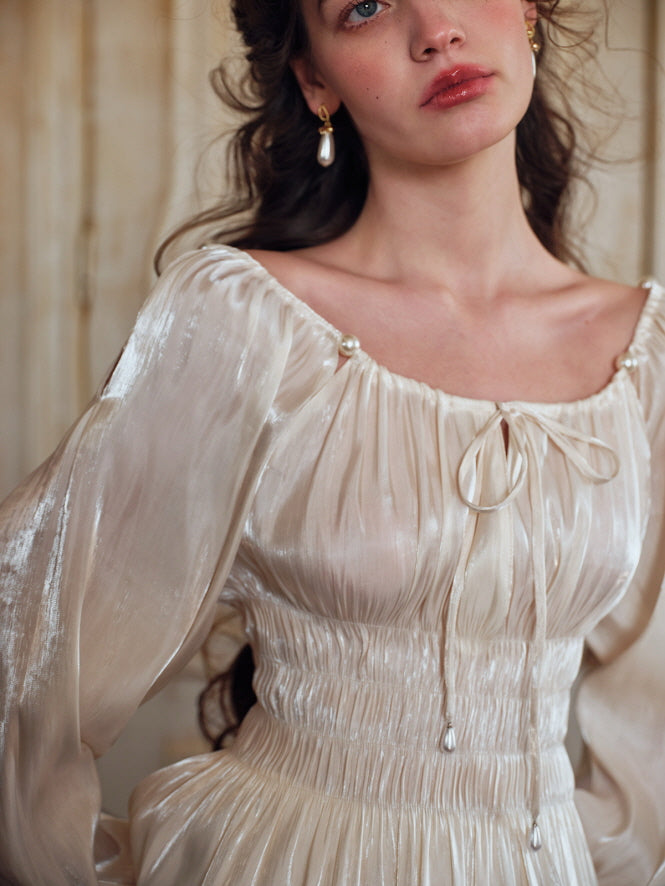 Close-up of an elegant ivory satin blouse featuring delicate puff sleeves and a cinched waist, styled with a cream skirt, set against a backdrop of antique artwork and classic decor.