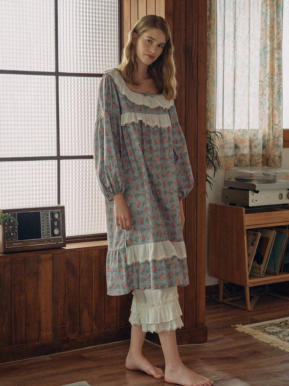 A young woman gently holding dried flowers while wearing a vintage-inspired floral loungewear set with delicate lace and ribbon details in soft blue tones.