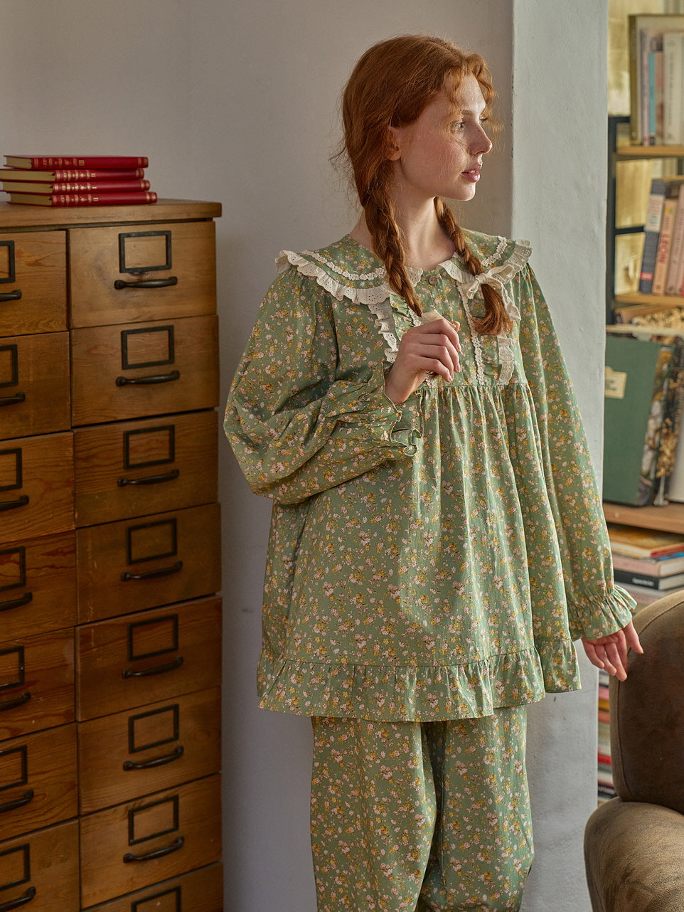 A dreamy, cottagecore-inspired scene with a model in a green floral loungewear set adorned with lace trim and ruffle accents, evoking nostalgic fairytale vibes.