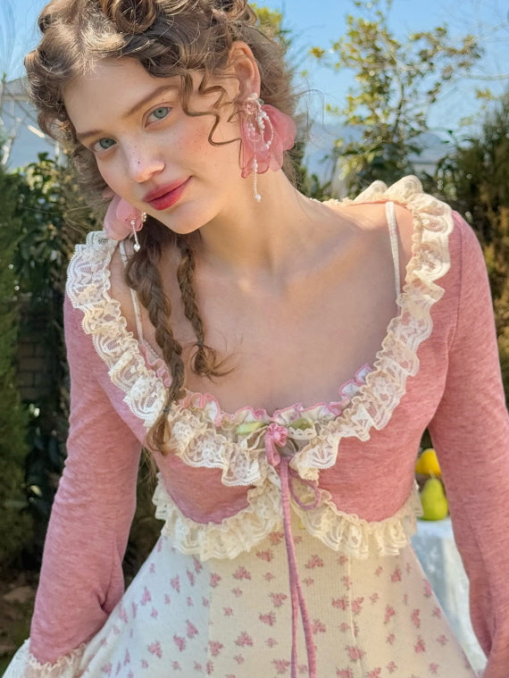 Delicate lace-trimmed cropped cardigan in a soft rose hue, paired with a floral knit dress adorned with ruffled details and pastel pink ribbon accents.