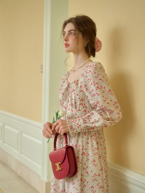 A romantic cottagecore outfit featuring a vintage-inspired floral dress with lace-up detail, styled with a pearl necklace and a small red handbag.