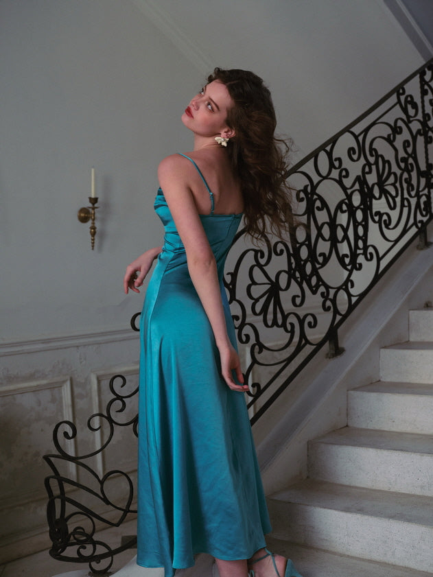 A woman stands elegantly in a turquoise satin dress adorned with a jeweled bodice, capturing a regal, fairytale aesthetic against a vintage staircase backdrop — romantic eveningwear, princess fashion, summer formal outfit.