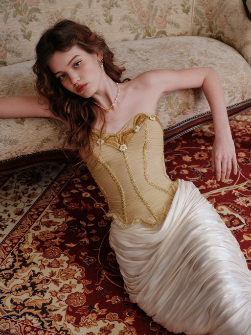 A romantic vintage-inspired gold corset with floral trim, paired with an ivory draped skirt, styled on a classic red and beige carpet for a timeless fairytale aesthetic.