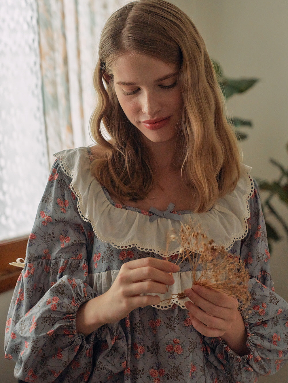 A serene scene featuring a woman in a cottagecore floral nightgown with ruffled lace accents, standing gracefully by a window in a cozy, vintage-styled room.