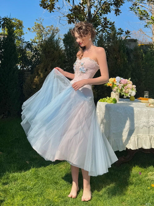 Woman wearing a pastel corset dress with a soft blue tulle skirt, gracefully holding the hem in a spring garden scene – elegant fairytale-inspired outfit