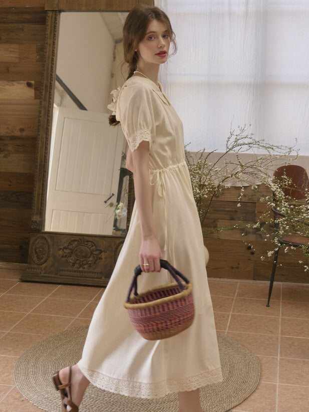 Side view of a woman walking gracefully in a cottagecore-style cream dress with delicate lace details, carrying a colorful woven basket.