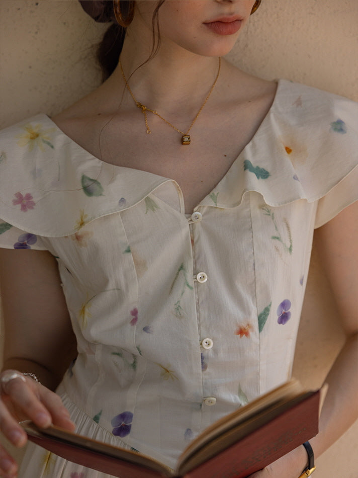 Close-up of a floral cottagecore dress with ruffled neckline and delicate button details, as the woman holds an open book, showcasing soft, romantic styling.