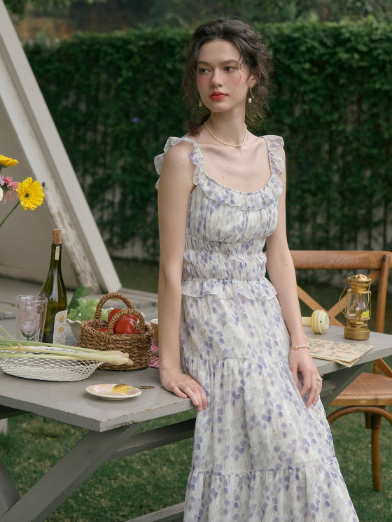 Woman sitting at a picnic table, dressed in a romantic cottagecore floral dress with ruffle details, creating a dreamy outdoor aesthetic.