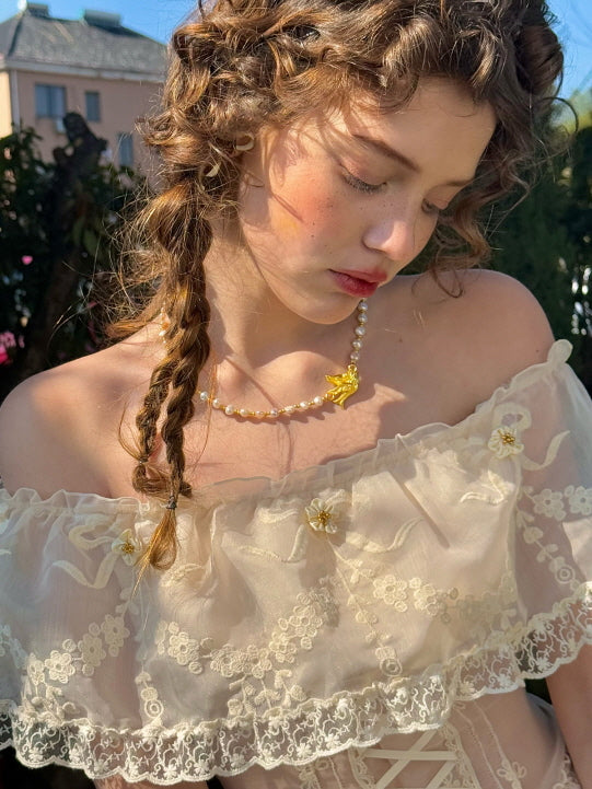 Close-up of romantic off-shoulder lace bodice with floral embroidery and yellow flower details, styled with pearl necklace and vintage curls – feminine fairytale aesthetic